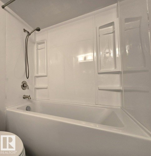 White bathtub and shower surround featuring integrated shelving, a brushed nickel showerhead, and matching tub filler - 60 Northwoods Village Nw, Edmonton, AB - Indoor Photo Showing Bathroom