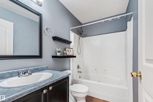 Bathroom featuring a white bathtub and shower surround, a vanity with an integrated sink, and wood-finish flooring - 16737 116 Street Nw, Edmonton, AB 
