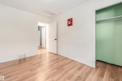 Spacious room with wood-finish flooring, white walls, and a built-in closet with shelving - 