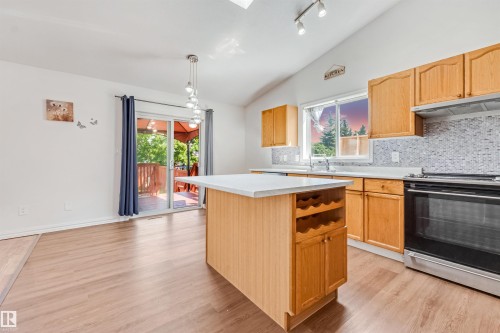 Kitchen featuring wood-finish flooring, light wood cabinetry, a mosaic tile backsplash, stainless steel appliances, and a central island with integrated wine storage - 16737 116 Street Nw, Edmonton, AB 