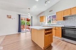 Kitchen featuring wood-finish flooring, light wood cabinetry, a mosaic tile backsplash, stainless steel appliances, and a central island with integrated wine storage - 