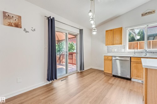 Kitchen area featuring wood-finish flooring, light wood cabinetry, and a stainless steel dishwasher - 16737 116 Street Nw, Edmonton, AB 