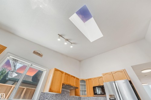 Kitchen featuring a ceiling skylight, track lighting, wood-finish cabinetry, built-in microwave, and stainless steel refrigerator - 16737 116 Street Nw, Edmonton, AB 