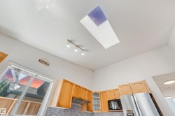 Kitchen featuring a ceiling skylight, track lighting, wood-finish cabinetry, built-in microwave, and stainless steel refrigerator - 