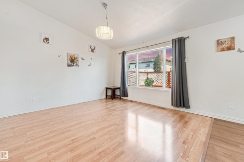Bright open-concept interior featuring wood-finish flooring, a large picture window, and a modern ceiling light fixture - 16737 116 Street Nw, Edmonton, AB 