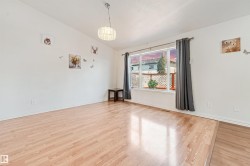 Bright open-concept interior featuring wood-finish flooring, a large picture window, and a modern ceiling light fixture - 