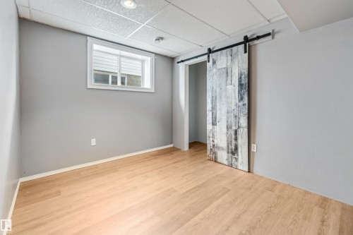 Room featuring wood-finish flooring, a white window frame, and a rustic barn door with black hardware - 16737 116 Street Nw, Edmonton, AB 