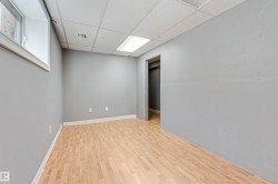 Room featuring wood-finish flooring, light gray walls, a dropped acoustic ceiling with integrated lighting, and a window with white trim - 