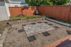 Backyard featuring a paver patio area with hexagonal pavers, gravel surfacing, a raised stone retaining wall, and a wooden privacy fence - 