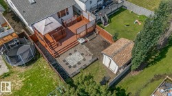 Multi-level rear deck with wood railing, featuring a lower patio with decorative pavers, and a detached shed with shingle roofing - 