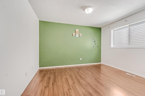 Spacious room featuring wood-finish flooring, a prominent green accent wall, and white trim - 16737 116 Street Nw, Edmonton, AB 