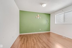 Spacious room featuring wood-finish flooring, a prominent green accent wall, and white trim - 