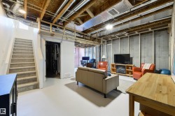 Open lower level featuring a light gray finished floor, exposed wood ceiling joists, and concrete foundation walls with wood framing - 