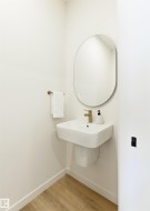 Bathroom with pedestal sink, elliptical mirror, and wood-finish flooring - 