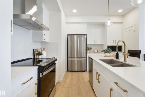 Modern kitchen featuring white cabinetry, stainless steel appliances, light wood-finish flooring, a kitchen island with sink, and contemporary brass hardware and fixtures - 323 Rankin Drive, St. Albert, AB - Indoor Photo Showing Kitchen With Double Sink With Upgraded Kitchen