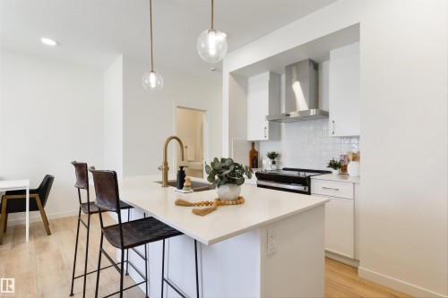 Kitchen island with a light-toned countertop and gold-finish faucet, illuminated by two clear globe pendant lights - 323 Rankin Drive, St. Albert, AB - Indoor Photo Showing Kitchen With Upgraded Kitchen
