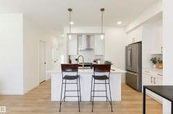 Contemporary kitchen featuring a white island, gold-tone hardware, stainless steel appliances, a tile backsplash, and light wood-finish flooring - 