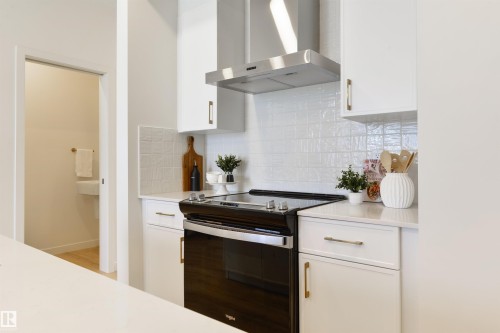 Modern kitchen featuring a black oven with a stainless steel range hood, white cabinetry, and white textured tile backsplash - 323 Rankin Drive, St. Albert, AB - Indoor Photo Showing Kitchen
