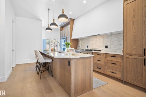 Gourmet kitchen featuring a large central island with seating, natural wood-finish cabinetry, light-toned countertops, a tile backsplash, and stainless steel appliances - 12304 62 Ave Nw, Edmonton, AB - Indoor Photo Showing Kitchen With Upgraded Kitchen