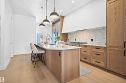 Gourmet kitchen featuring a large central island with seating, natural wood-finish cabinetry, light-toned countertops, a tile backsplash, and stainless steel appliances - 
