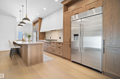 Contemporary kitchen featuring light wood-finish cabinetry, a large center island with seating, pendant lighting, stainless steel appliances, and wood-finish flooring - 12304 62 Ave Nw, Edmonton, AB - Indoor Photo Showing Kitchen With Upgraded Kitchen