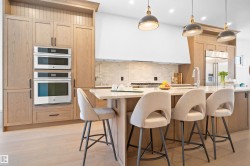 Bright kitchen featuring light wood-finish cabinetry, a large kitchen island with a light-toned countertop, stainless steel double wall ovens, and pendant lighting fixtures - 