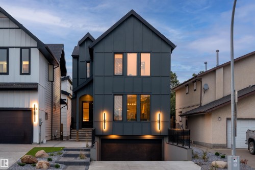 Contemporary dark-toned exterior with vertical panel siding, prominent gable roofline, integrated garage, and illuminated entryway - 12304 62 Ave Nw, Edmonton, AB - Outdoor With Facade