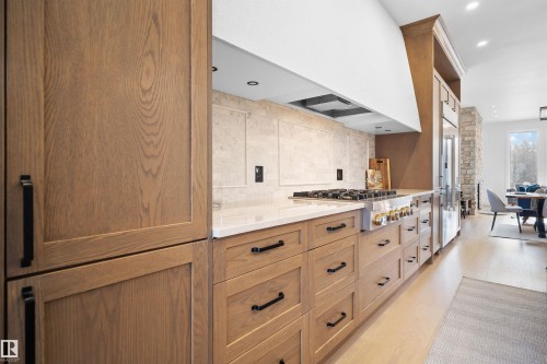 Gourmet kitchen featuring light wood-finish cabinetry with black hardware, white countertops, a large professional-grade range with a custom hood, and a built-in stainless steel refrigerator - 12304 62 Ave Nw, Edmonton, AB - Indoor Photo Showing Other Room