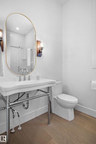 Bathroom featuring a pedestal sink with chrome fixtures, a gold-framed oval mirror, and wood-finish flooring - 12304 62 Ave Nw, Edmonton, AB - Indoor Photo Showing Bathroom