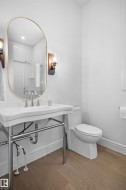Bathroom featuring a pedestal sink with chrome fixtures, a gold-framed oval mirror, and wood-finish flooring - 