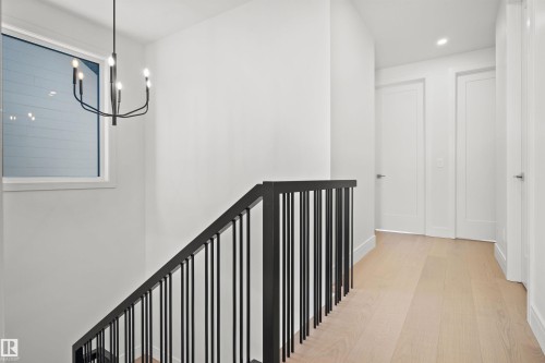 Staircase featuring a modern black railing system, wood-finish flooring, white walls, and a contemporary black chandelier - 12304 62 Ave Nw, Edmonton, AB - Indoor Photo Showing Other Room