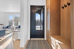 Entryway featuring a black paneled door with glass inserts, light wood-finish flooring, and a built-in wood bench with storage drawers - 