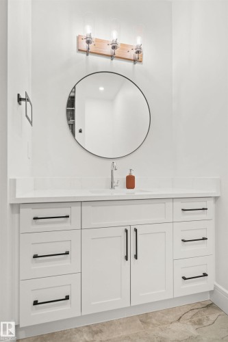 Bathroom vanity featuring white cabinetry, black hardware, an undermount sink, and a circular mirror - 12304 62 Ave Nw, Edmonton, AB - Indoor Photo Showing Bathroom