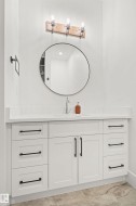 Bathroom vanity featuring white cabinetry, black hardware, an undermount sink, and a circular mirror - 