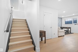 Hardwood stairs with a dark handrail, overhead recessed lighting, and a window providing natural illumination - 