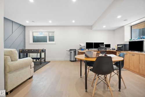 Open-concept room featuring light wood-finish flooring, recessed lighting, a modern accent wall with geometric paneling, and two windows - 12304 62 Ave Nw, Edmonton, AB - Indoor