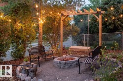 Outdoor entertainment area featuring a stone-clad fire pit, two black metal benches, a wooden pergola with an attached swing, and string lighting - 