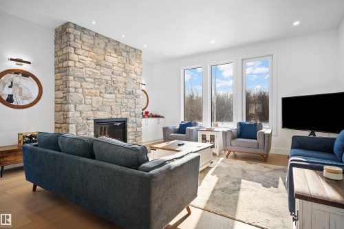 Living area featuring a stone-clad fireplace with an integrated firebox, wood-finish flooring, recessed lighting, and a wall of three vertical windows - 12304 62 Ave Nw, Edmonton, AB - Indoor Photo Showing Living Room With Fireplace