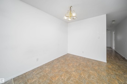 Dining area featuring a five-light brass chandelier, white painted walls, and square terracotta-toned floor tiles - 12041/43 67 St Nw Nw, Edmonton, AB - Indoor Photo Showing Other Room