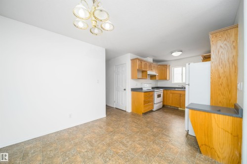 Kitchen area featuring light wood cabinetry, dark countertops, and tile-finish flooring - 12041/43 67 St Nw Nw, Edmonton, AB - Indoor Photo Showing Kitchen