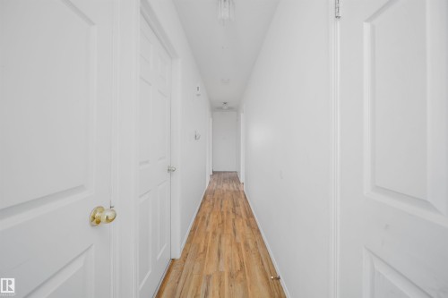 Hallway featuring wood-finish flooring, white walls, and multiple paneled doors - 12041/43 67 St Nw Nw, Edmonton, AB - Indoor Photo Showing Other Room