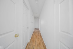 Hallway featuring wood-finish flooring, white walls, and multiple paneled doors - 