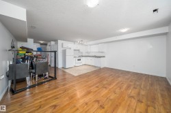 Open-concept living area featuring wood-finish flooring, a white kitchen with stone-finish countertops, white appliances, and ample wall space - 