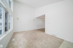 Vaulted ceiling room with large multi-pane windows, neutral-toned carpeting, and a wall archway - 