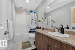 Full bathroom featuring a white tub and shower combination with tiled surround, a wood-finish vanity with an integrated sink, a speckled countertop, and a large wall-mounted mirror - 