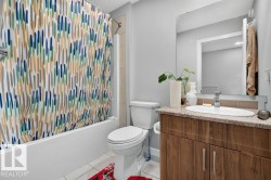 Bathroom featuring a wood-finish vanity with an oval undermount sink, a tiled backsplash, and a large wall-mounted mirror - 