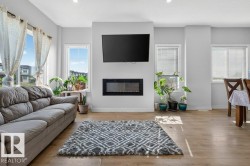 Open-concept living area featuring light wood-finish flooring, recessed lighting, and an electric fireplace with a wall-mounted television above - 