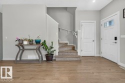 Entryway featuring light wood-finish flooring, a white paneled front door with clear glass inserts, and a carpeted staircase with white handrails - 