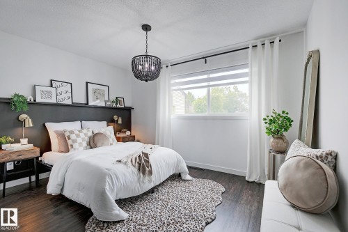 Bedroom featuring dark wood-finish flooring, a contemporary black beaded chandelier, and a built-in dark panel headboard with an integrated shelf - 19F Meadowlark Village Nw, Edmonton, AB - Indoor Photo Showing Bedroom