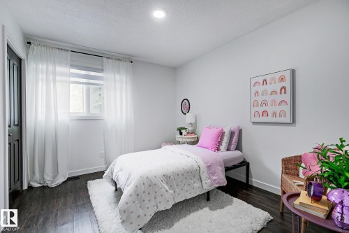 Bedroom with dark wood-finish flooring and a single window featuring sheer white curtains - 19F Meadowlark Village Nw, Edmonton, AB - Indoor Photo Showing Bedroom